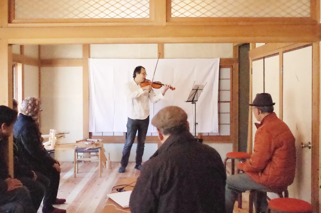 和室でバイオリンを演奏する男性と、それを鑑賞する人々